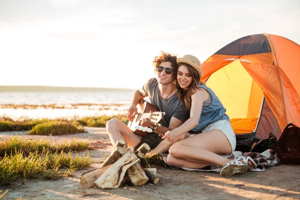 Couple playing guitar and frying marshmallows on bonfire together — Stock Photo, Image