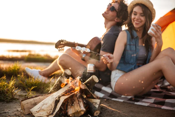 Couple playing guitar and frying marshmallows on bonfire