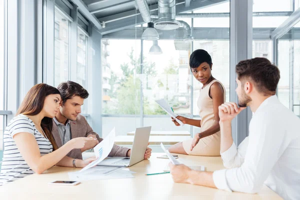 Quatre jeunes entrepreneurs concentrés travaillant avec des documents et utilisant un ordinateur — Photo