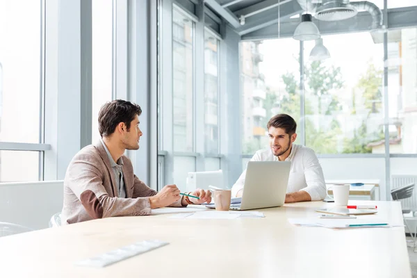 Two busnessmen with laptop sitting and talking in office — Stock Photo, Image