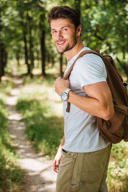 Man holding backpack and walking in forest clipart