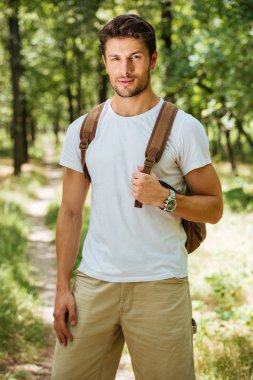 Man holding backpack and standing in forest clipart
