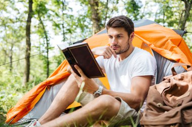 Oturma ve ormandaki kitap okuma düşünceli genç adam turizm