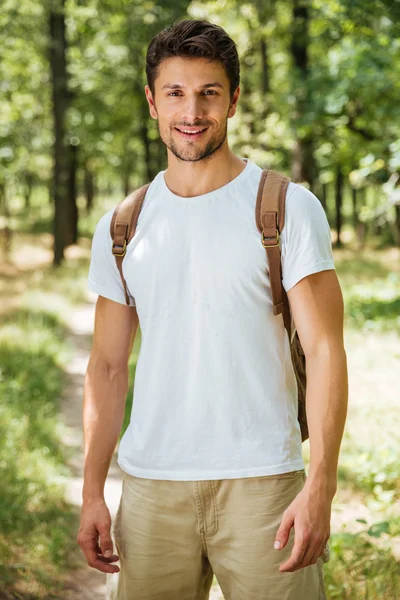 Χαρούμενος νεαρός άνδρας με σακίδιο στέκεται στο δάσος — Φωτογραφία Αρχείου