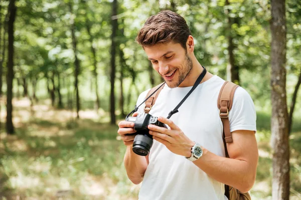 Smiling man photographer using modern photo camera in forest — Stock Photo, Image