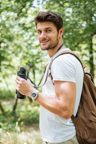 Hombre con mochila de pie y sosteniendo binoculares en el bosque —  Fotos de Stock