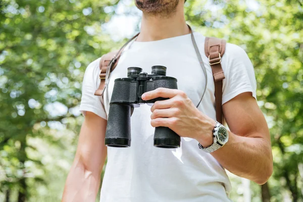 Homem com mochila em pé e segurando binóculos na floresta — Fotografia de Stock