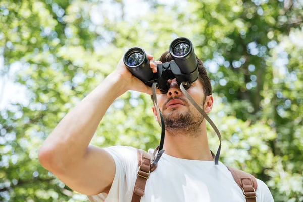 Uomo con zaino guardando attraverso il binocolo nella foresta — Foto Stock
