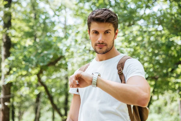 Serious man with backpack checking time and looking at watch — Stock Photo, Image