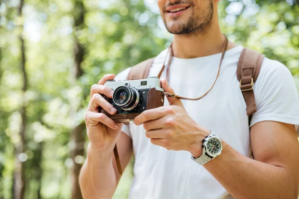 Hombre sonriente con mochila tomando fotos usando cámara vintage al aire libre — Foto de Stock