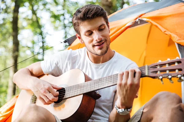Glücklicher junger Mann sitzt im Wald und spielt Gitarre — Stockfoto