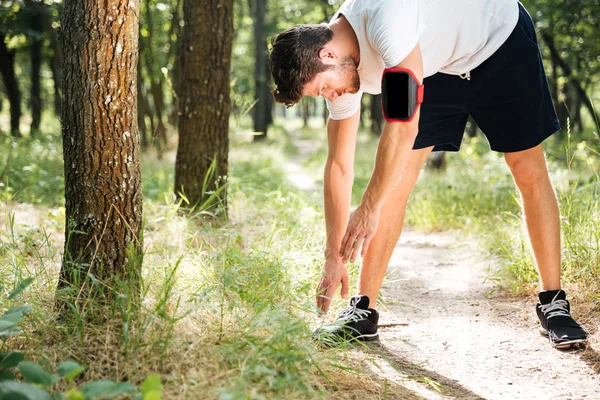 Man athlete using smartphone in handband working out in forest — Stock Photo, Image