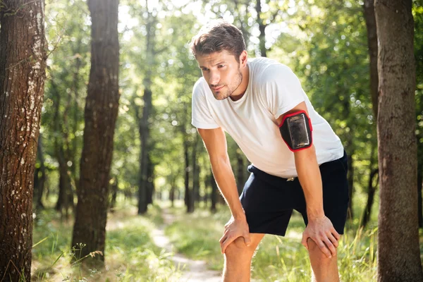 Tired young sportsman standing and relaxing after running in forest — Stock Photo, Image