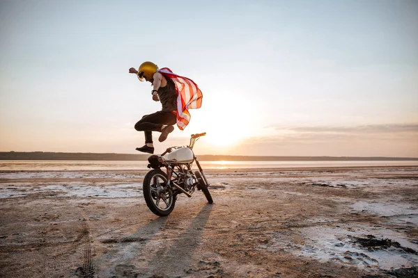 Brutal homem pulando sobre sua moto ao pôr do sol — Fotografia de Stock