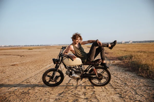 Joven hombre brutal acostado en su motocicleta y posando — Foto de Stock