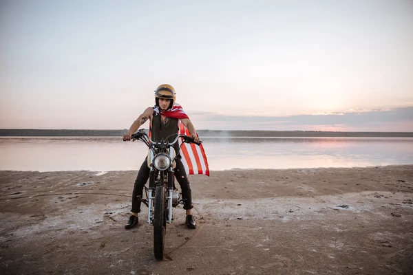 Man in golden helmet and american flag cape driving motorcycle