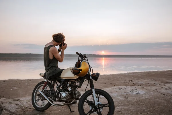 Человек фотографируется с камерой, сидя на мотоцикле — стоковое фото