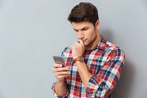 Fundersam ung man i rutig skjorta med mobiltelefon — Stockfoto