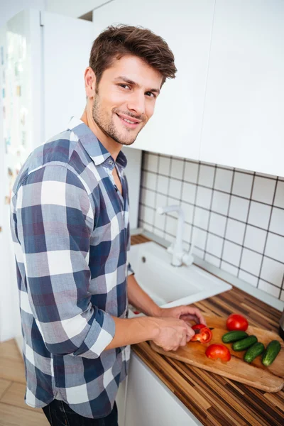 Jovem feliz cortando legumes para salada na cozinha — Fotografia de Stock