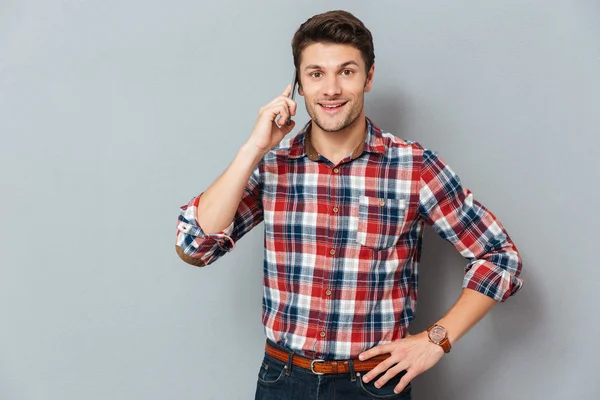 Sonriente joven guapo de pie y hablando por teléfono celular — Foto de Stock