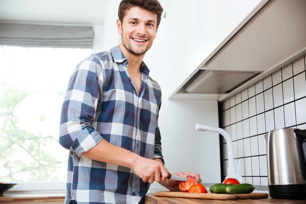 Jovem alegre cortando legumes para salada na cozinha — Fotografia de Stock