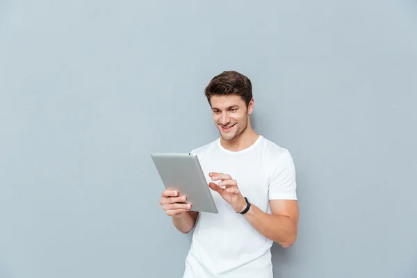 Happy attractive young man standing and using tablet — Stock Photo, Image