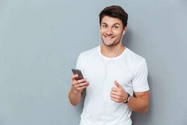 Joven feliz escuchando música y mostrando los pulgares hacia arriba — Foto de Stock