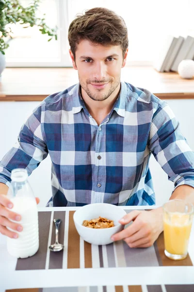 Homem sentado e comendo cereais com leite na cozinha — Fotografia de Stock