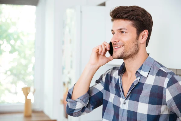 Smiling handsome young man talking on mobile phone at home — Stock Photo, Image