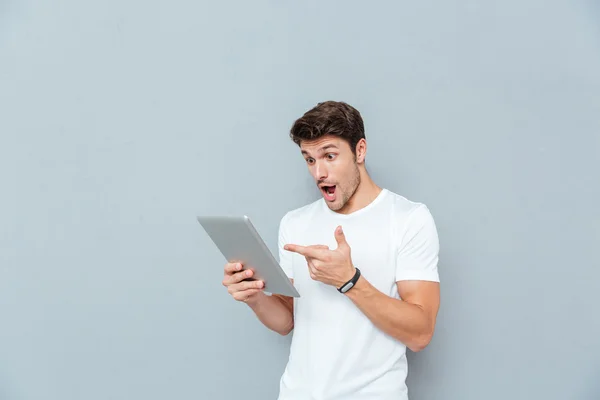 Giovane uomo sorpreso che tiene e punta su tablet — Foto Stock