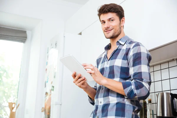 Hombre con camisa a cuadros usando tableta en la cocina — Foto de Stock