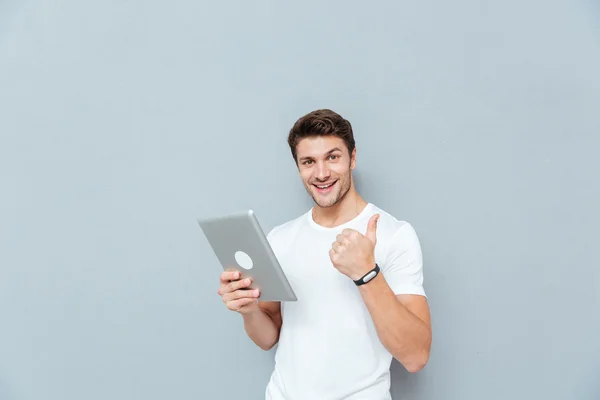 Joven alegre usando la tableta y mostrando los pulgares hacia arriba — Foto de Stock