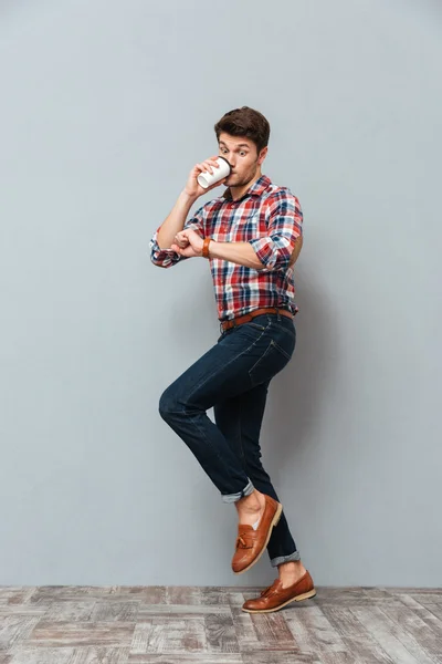 Wondered young man drinking takeaway coffee and looking at wristwatch — Stock Photo, Image