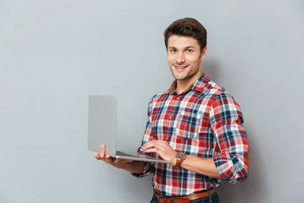 Happy young man in checkered shirt standing and holding laptop — Stock Photo, Image