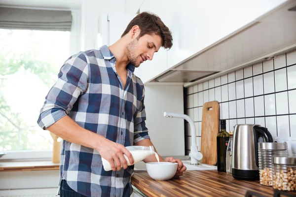 Homem derramando leite em tigela para o café da manhã na cozinha — Fotografia de Stock