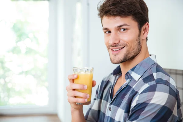 Sonriente joven bebiendo jugo fresco en la cocina —  Fotos de Stock