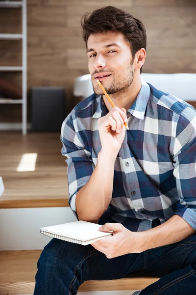 Thoughtful young man with notepad sitting and thinking at home — Stock Photo, Image