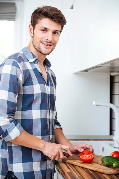 Souriant jeune homme coupant des légumes sur la cuisine — Photo