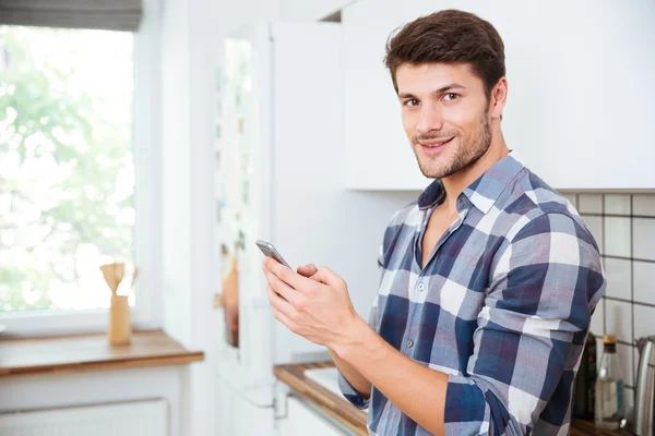 キッチンで携帯電話を使用して幸せな若い男 — ストック写真