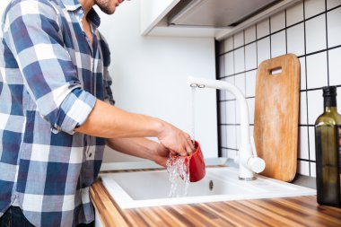 Man in checkered shirt washing dishes on the kitchen clipart