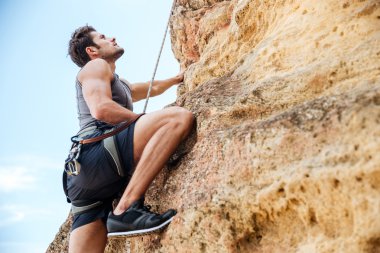 Young man climbing a steep wall in mountain clipart