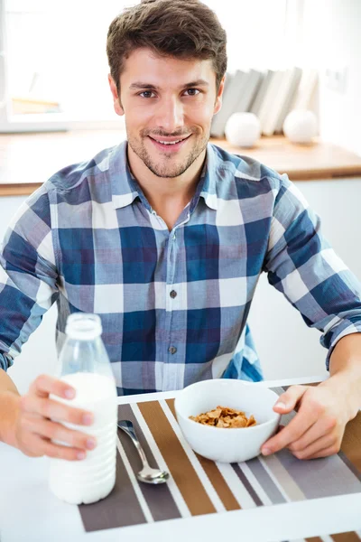 キッチンのテーブルにミルクが付いている穀物を食べている男 — ストック写真