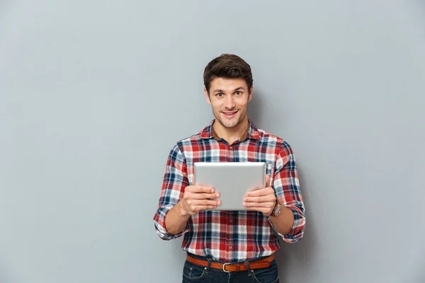 Smiling attractive young man in checkered shirt using tablet — Stock Photo, Image