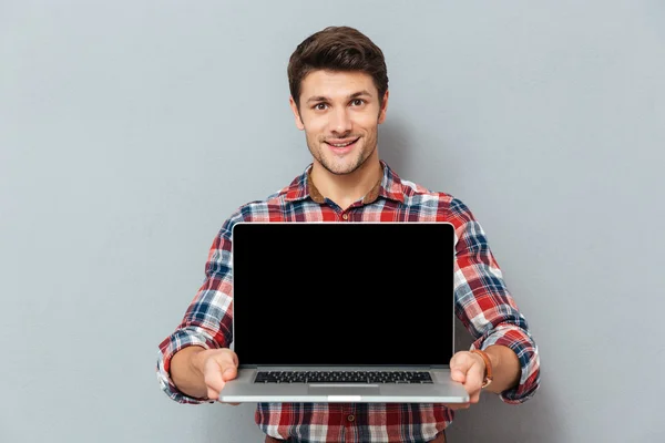 Sonriente joven con camisa a cuadros sosteniendo la pantalla en blanco portátil — Foto de Stock