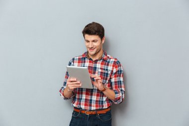 Mutlu genç adam ayakta ve tablet kullanarak ekose gömlekli