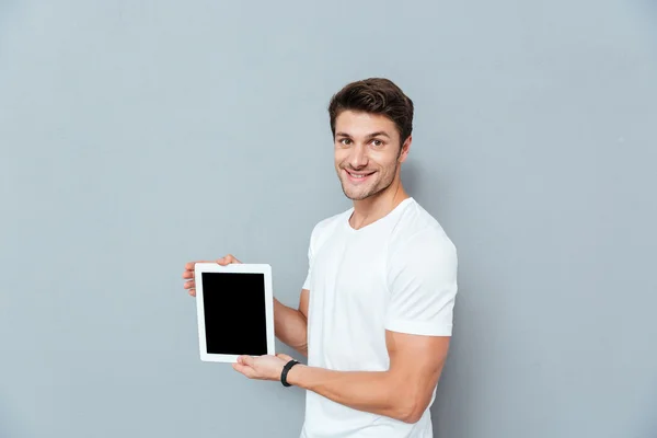 Sonriente joven guapo de pie y sosteniendo la tableta de pantalla en blanco — Foto de Stock