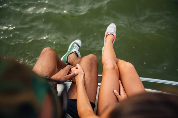 Nogi Młoda para w trampki siedzi w pobliżu morza — Zdjęcie stockowe