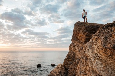 Denizin kenarında dağ kayada duran genç sporcu