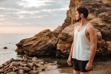 Denizin kenarında kayalık sahilde duran genç sporcu