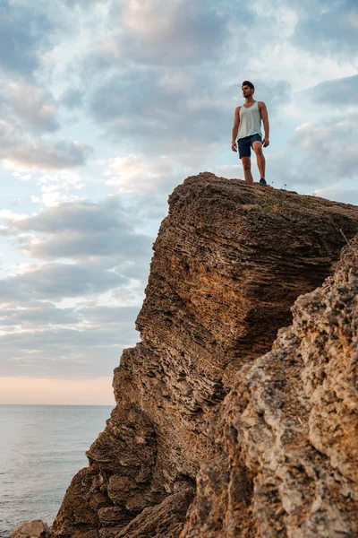 Νεαρός αθλητής που στέκεται στο βουνό βράχο δίπλα στη θάλασσα — Φωτογραφία Αρχείου